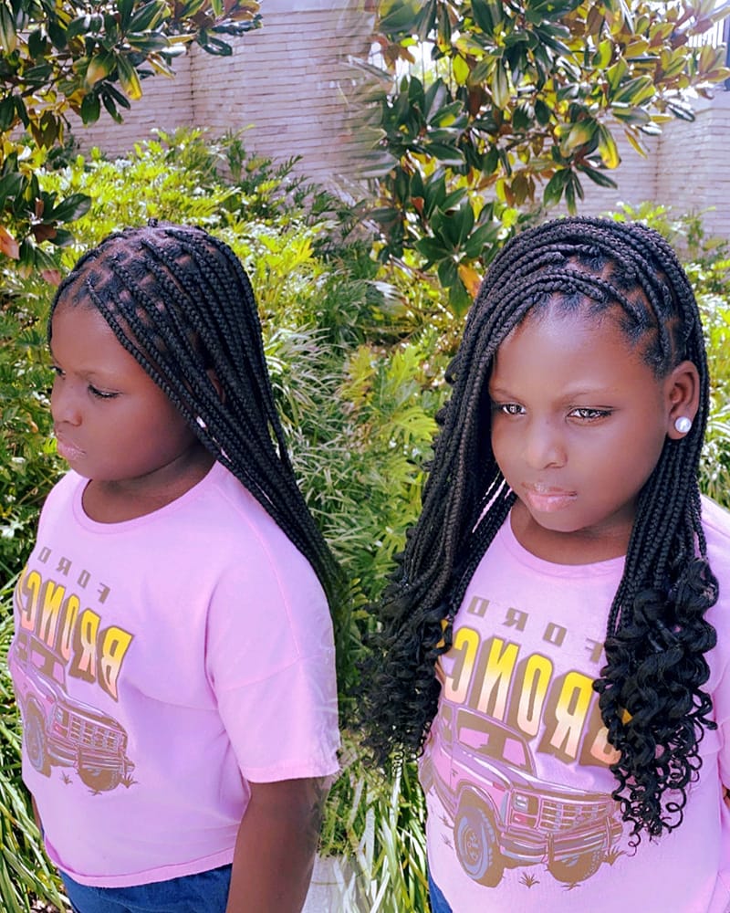 African American Kid Wearing Goddess Box Braids. The Kid is showing her hairstyle from the front and side.