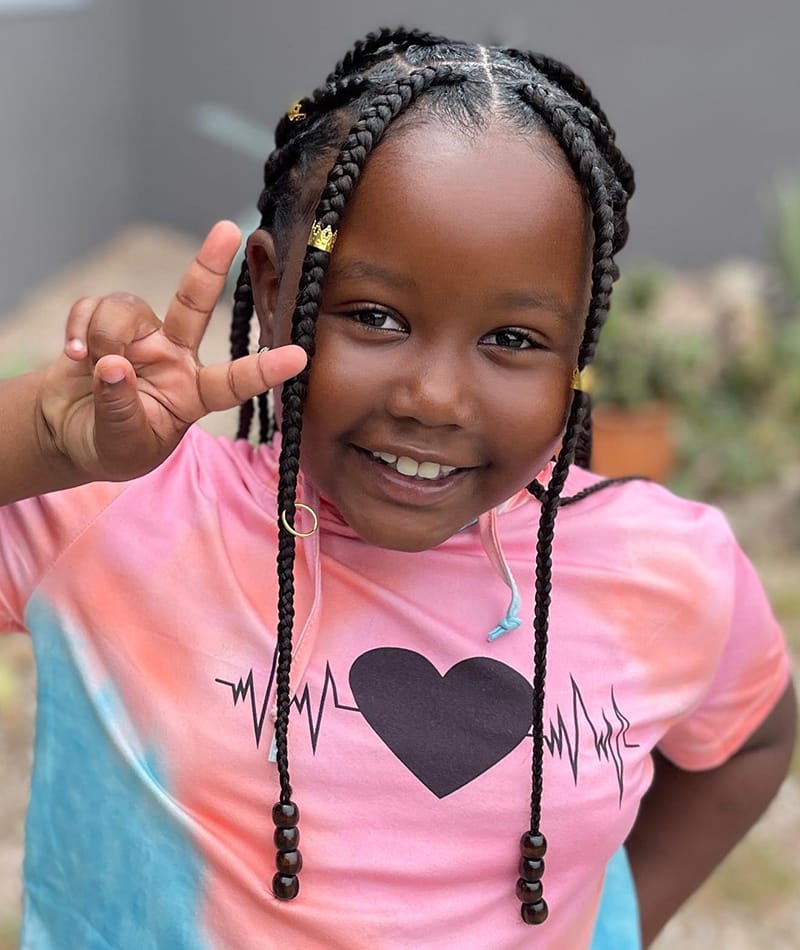 A cute 7 year old kid wearing cute box braids hairstyle with golden haircuffs and black beads.