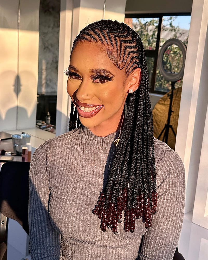 Woman wearing a back-length braided hairstyle. The braids are adorned with beautiful Fulani Beads.