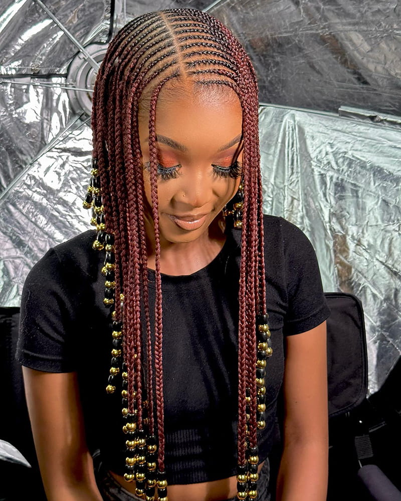 Woman wearing Braids of Burgundy Color. The braids are adorned with beads. This braid idea was invented by the Fulani people.