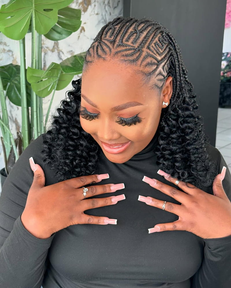 An African American woman is showing her braided Curls. She is wearing a Fulani braids hairstyle. And at the end of her braids, there are curly extensions.