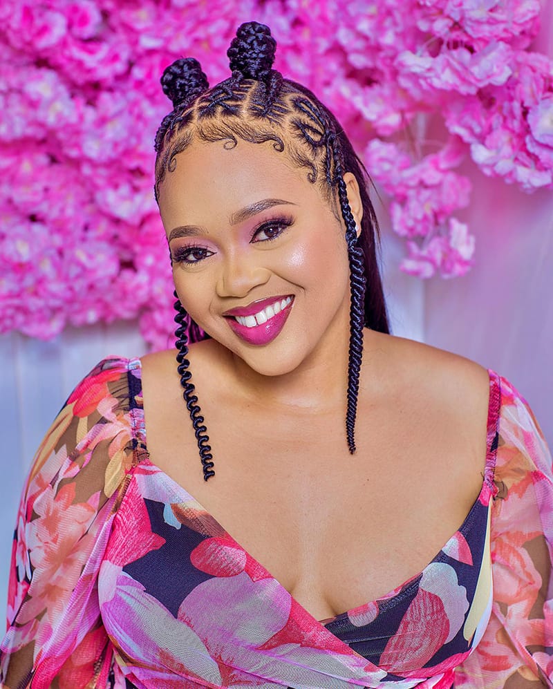 An African American woman is wearing a braided hairstyle with two braided knots on the top of her head.