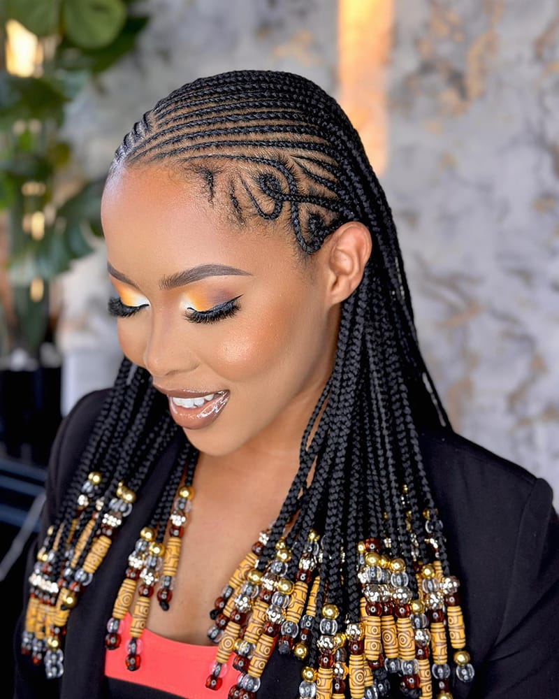 A Beautiful African American Woman is Wearing a Braided hairstyle. The Hairstyle is Fulani Inspired Braid Style. The Braids Contain Different Types of Beads like Glass Beads and Wooden Beads.