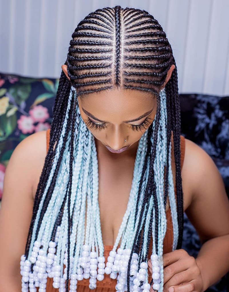 A woman wearing a horizontal Fulani Braids Hairstyle. The braids are colored black and white. At the same. the braids are adorned with white beads