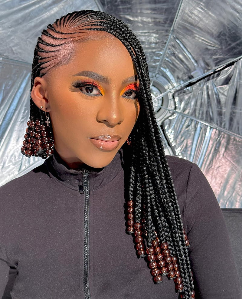 Woman Wearing a side-part braided hairstyle. The Hairstyle is adorned with dark beads. And the hairstyle is originated from the Fulani people of West Africa.